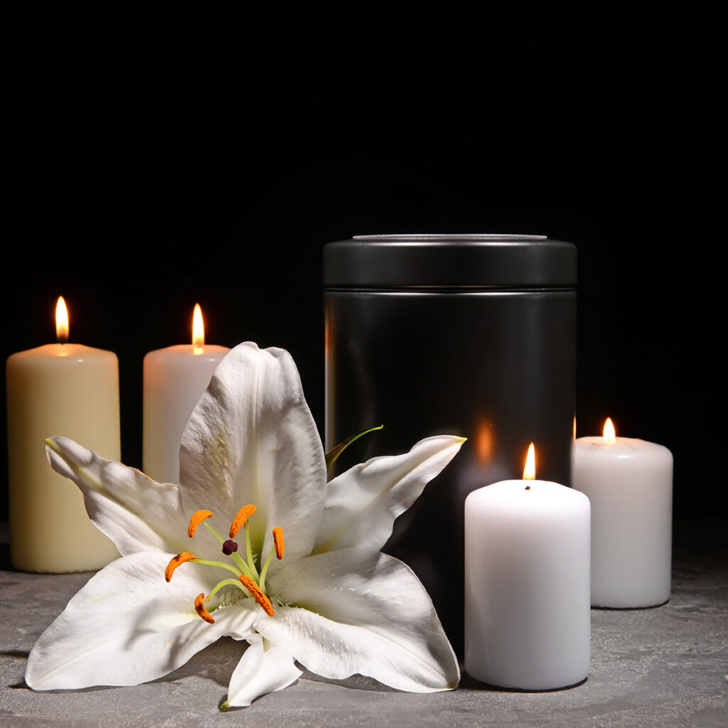 Elegant cremation urn next to a fresh flower and four candles, symbolising remembrance and peace