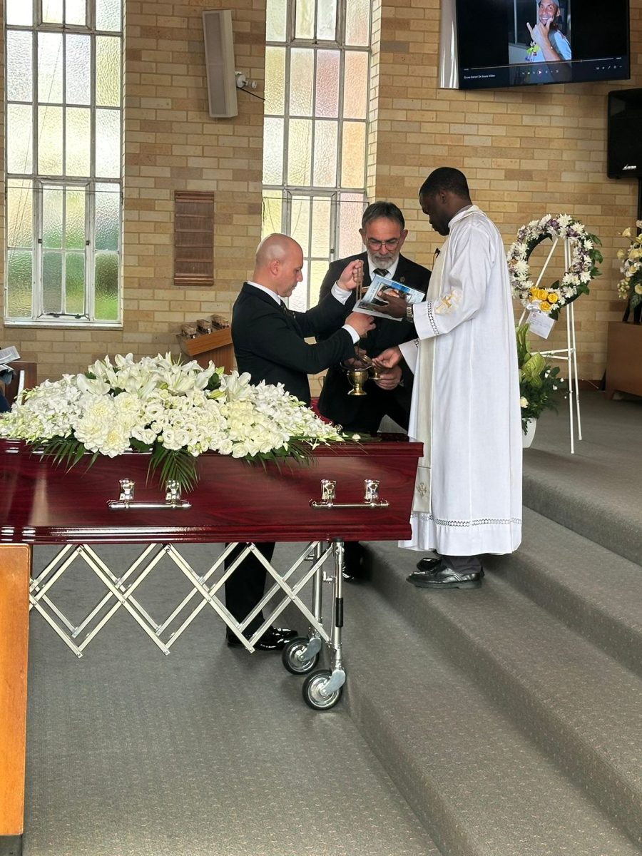 Catholic priest conducting a funeral service next to a coffin inside a Sydney church